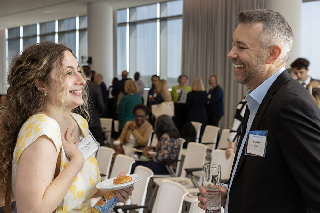 Woman on left in yellow shirt talking to a man on the right in a blue shirt and dress jacket.