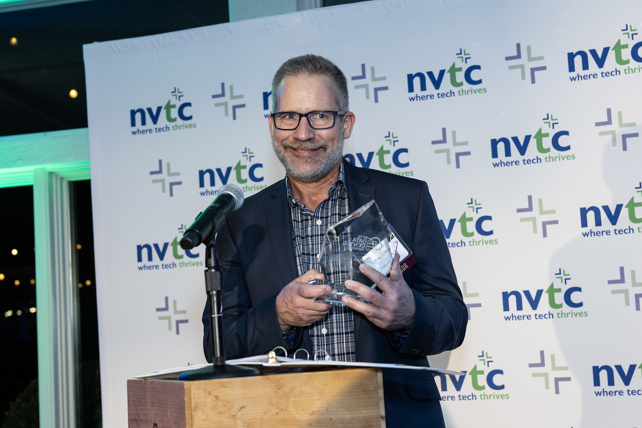 A man in a dark blue blazer in front of an NVTC step-and-repeat receiving the DAta Center Award.